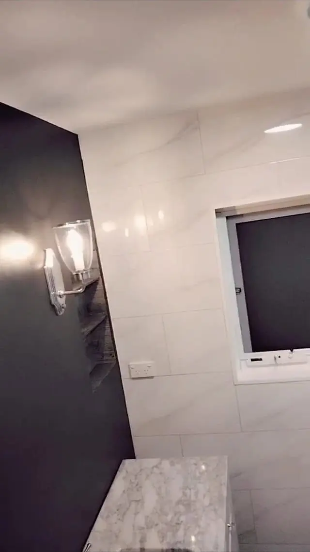 Bathroom with a dark feature wall, wall sconce and white marble-look tiles