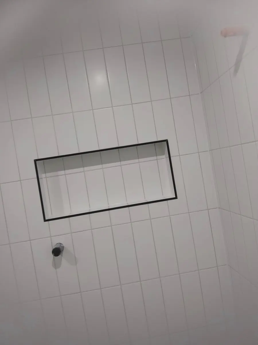 Shower niche finished with a black metal trim in vertical white tile